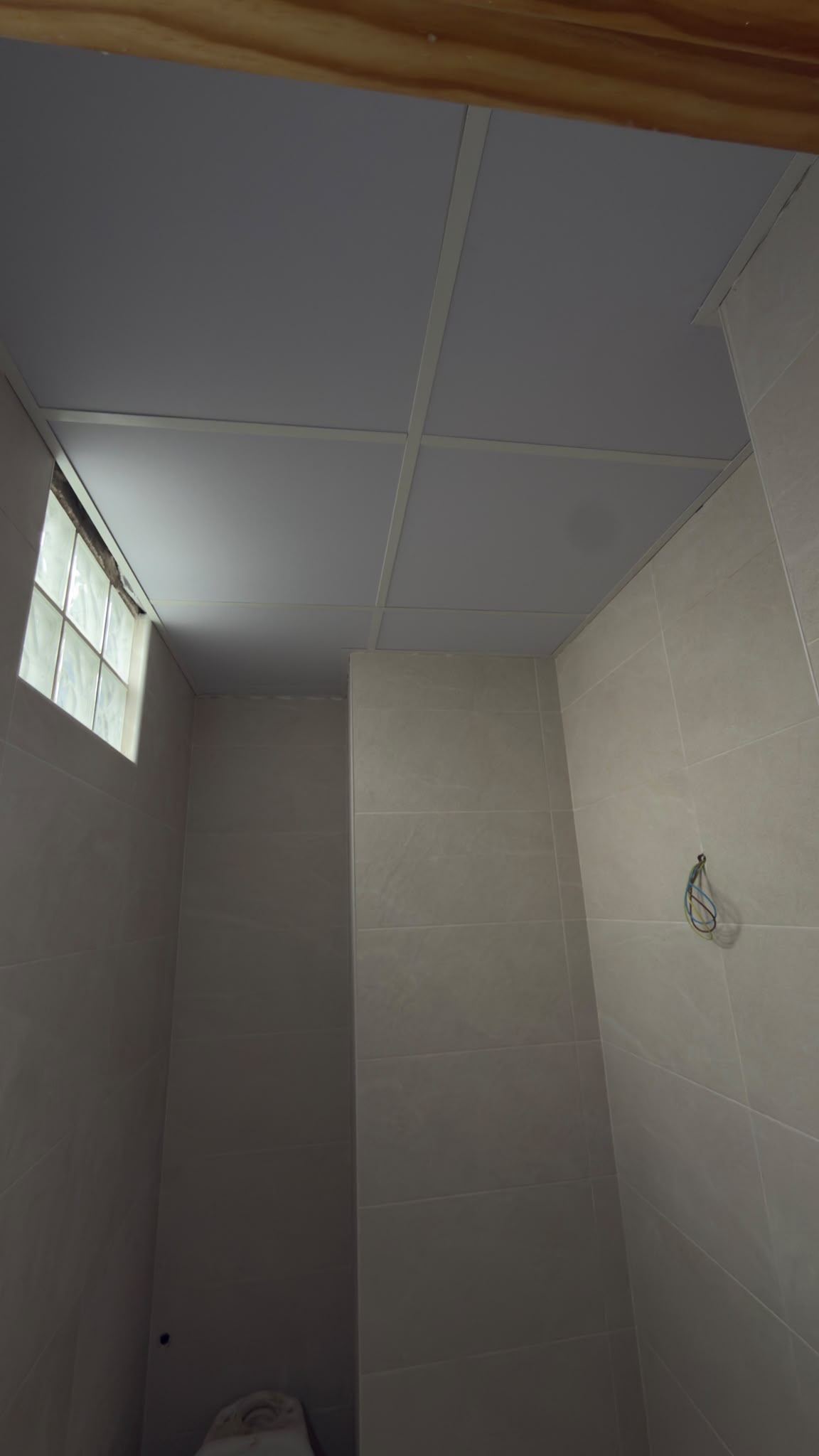 Baño alicatado con techo registrable de placas blancas y ventana de pavés