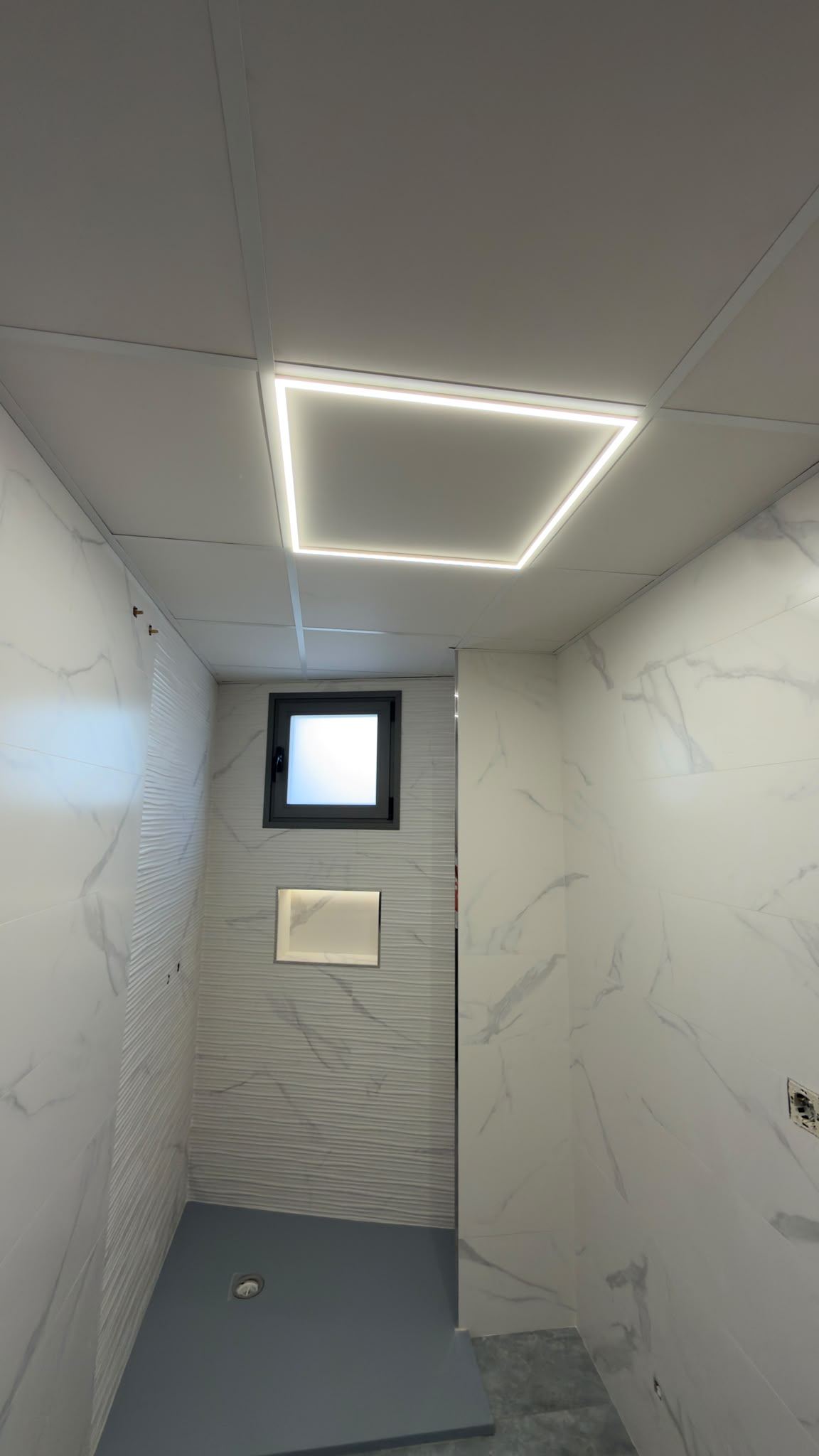 Baño con techo registrable de placas y un marco cuadrado de luz LED, ducha con hornacina bajo la ventana