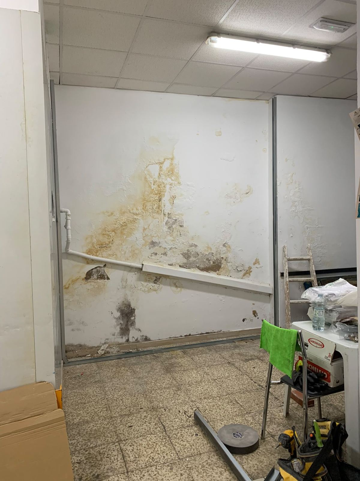 Pared de un local con manchas de humedad y la pintura levantada, con la perfilería empezando a montarse