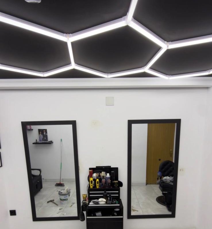 Techo negro de una barbería con retícula hexagonal de líneas LED sobre los espejos
